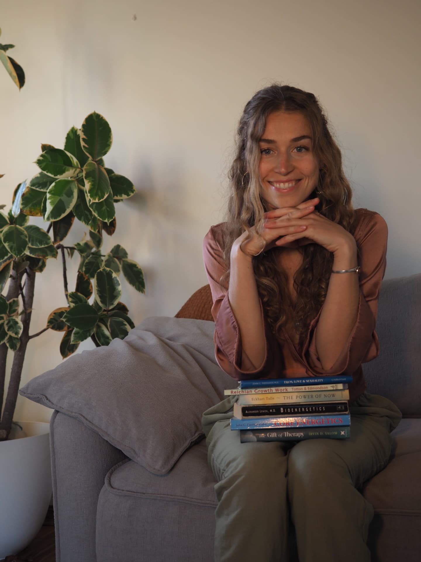 Anna-Lena sitting on a couch with a stack of books on her lap, smiling with her chin resting on her hands